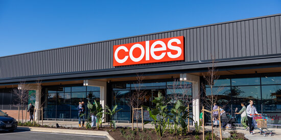The Coles supermarket entrance at The Palms Shopping Village, with landscaped garden beds and parking in the foreground.