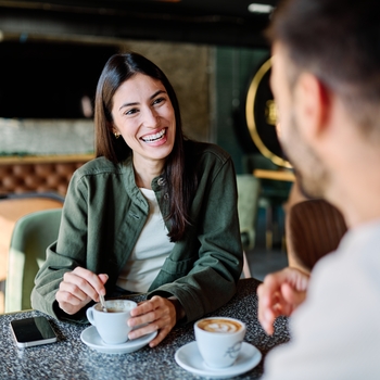 A woman laughs while enjoying a coffee with a friend at a cafe at The Palms Shopping Village.