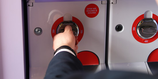 A person inserts a coin into a brightly coloured prize vending machine with a 'Spin Me, Round & Round' dial.